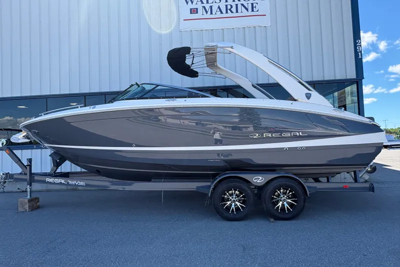 The Image of 2027 Regal LS6 boat on trailer outside dealership, sleek design, gray and white finish. - 1