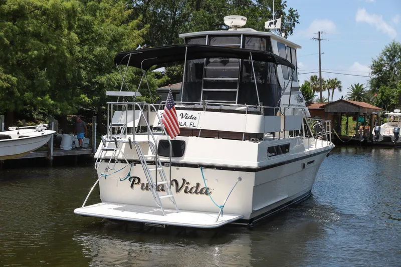 Slide: The Image of 1987 Hatteras 40 Double Cabin yacht named "Pura Vida" docked in a scenic canal. - 2