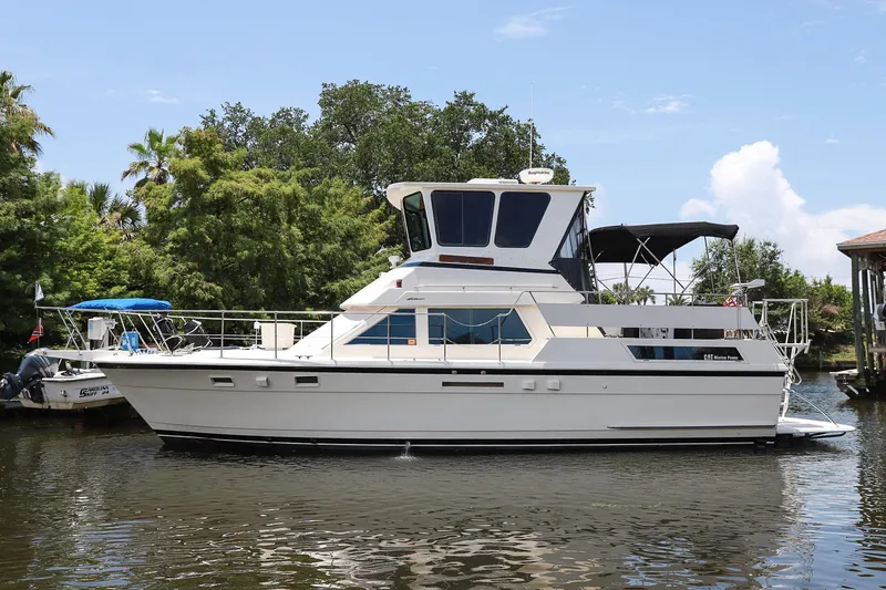 The Image of 1987 Hatteras 40 Double Cabin yacht on a calm river, surrounded by lush greenery. - 0