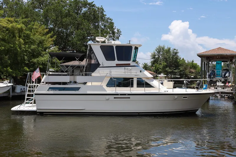 Slide: The Image of 1987 Hatteras 40 Double Cabin yacht docked on a serene waterway, surrounded by lush greenery. - 1