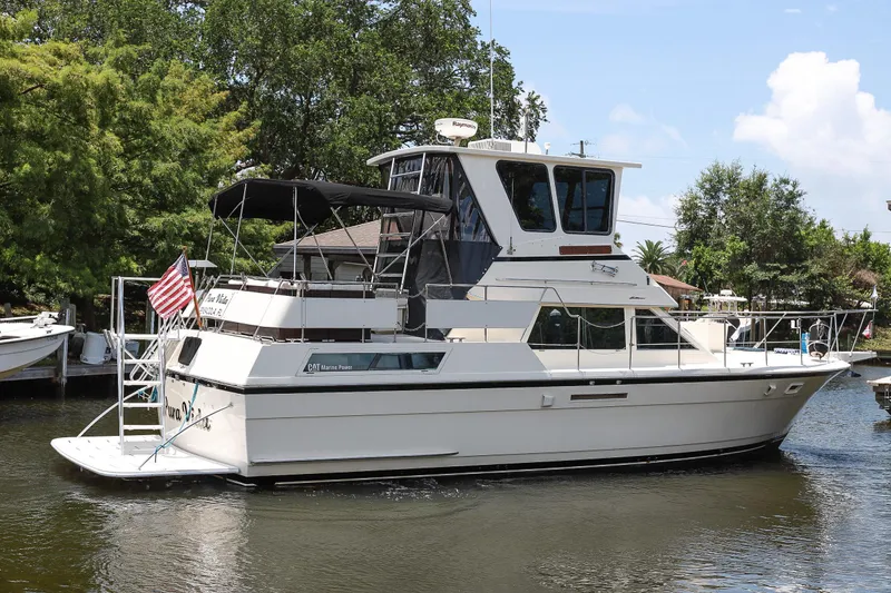 Slide: The Image of 1987 Hatteras 40 Double Cabin yacht docked on a calm waterway, surrounded by trees. - 3