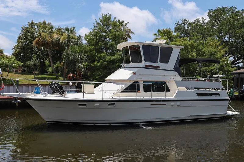Slide: The Image of 1987 Hatteras 40 Double Cabin yacht docked on a sunny day, surrounded by lush greenery. - 10