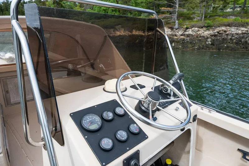 Slide: The Image of 1989 Ellis 24 Open boat dashboard with steering wheel and gauges, near a scenic shoreline. - 26
