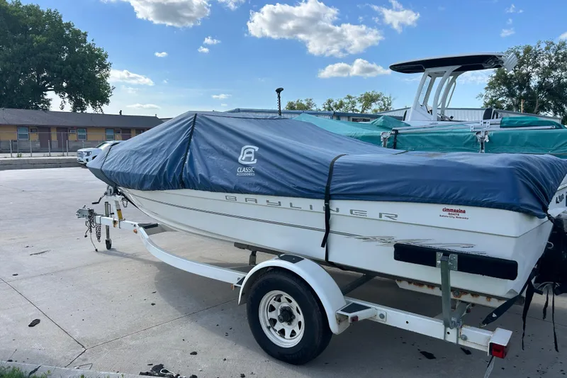 Slide: The Image of 1999 Bayliner 1954 Capri boat on trailer, covered with blue tarp, parked outdoors. - 10