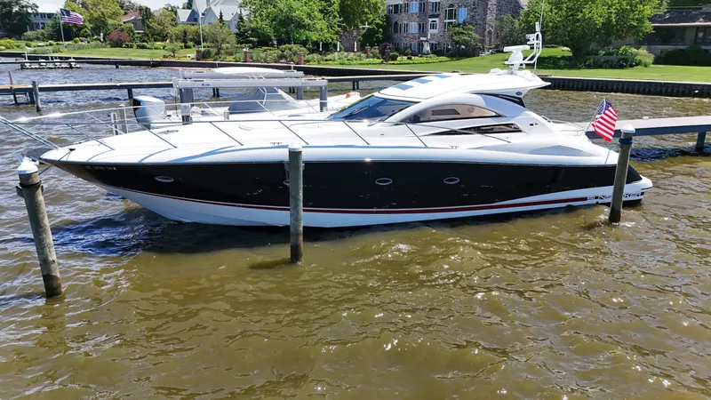 The Image of A 2008 Sunseeker Portofino 53 docked in calm waters, surrounded by greenery and houses. - 0