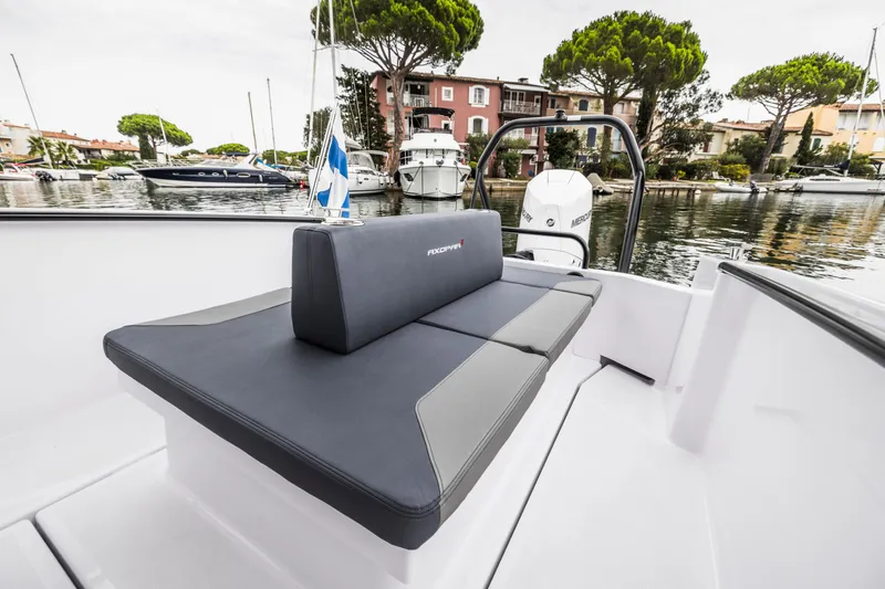 Slide: The Image of The 2023 Axopar 25 Cross Top is docked in a calm harbor with surrounding buildings. - 19