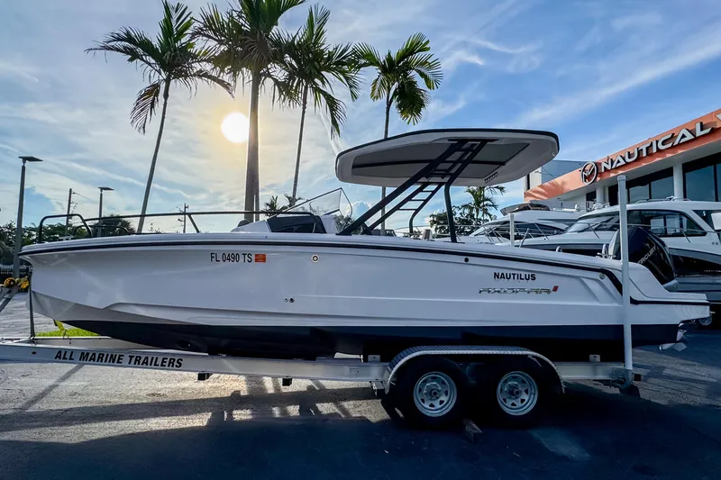 Slide: The Image of 2023 Axopar 25 Cross Top boat on trailer, displayed outdoors with palm trees and dealership. - 1
