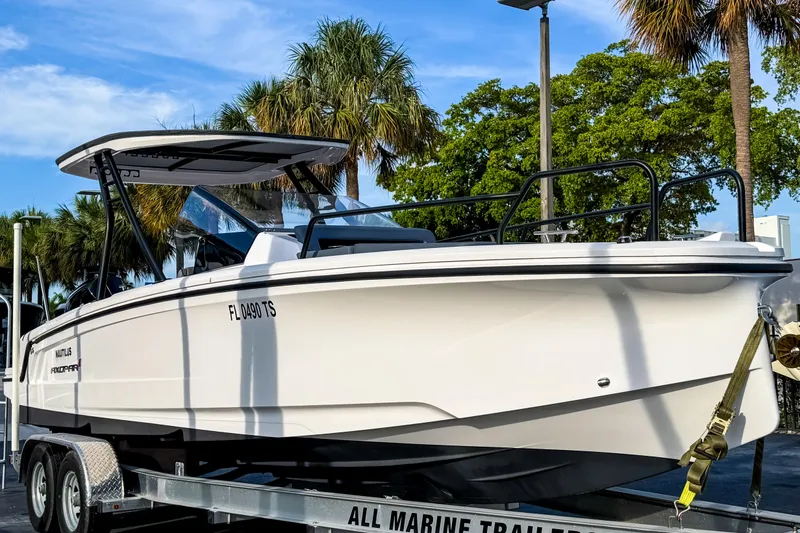 Slide: The Image of 2023 Axopar 25 Cross Top boat on trailer, surrounded by palm trees. - 2
