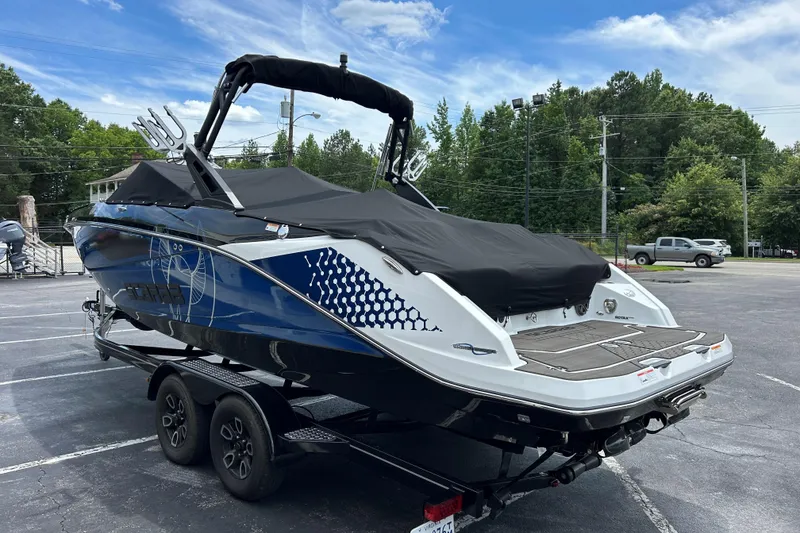 Slide: The Image of 2023 Scarab 255 Wake ID boat on trailer, covered, in parking lot with trees and sky background. - 30