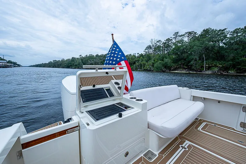 Slide: The Image of 2023 Hinckley Sport Boat 40 X with American flag, spacious deck, and scenic river view. - 7