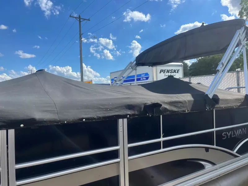 Slide: The Image of A 2015 Sylvan 8522 CNF pontoon boat with a black cover, parked under a blue sky. - 20