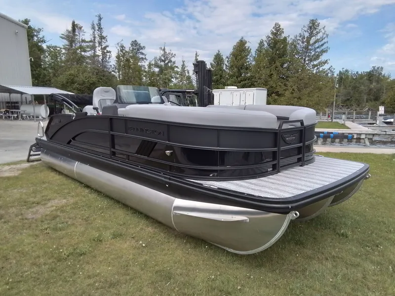 The Image of A sleek Bennington pontoon boat sits on grass, surrounded by trees and a building. - 1