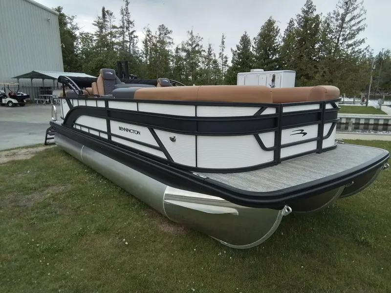 The Image of A 2026 Bennington 23SSRSF pontoon boat is parked on grass beside a building. - 1