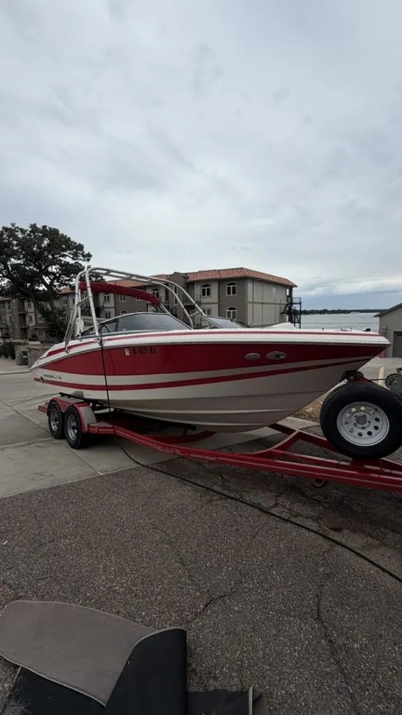 The Image of A 2004 Regal 2100 boat on a trailer, featuring a red stripe pattern, is parked on land. - 0