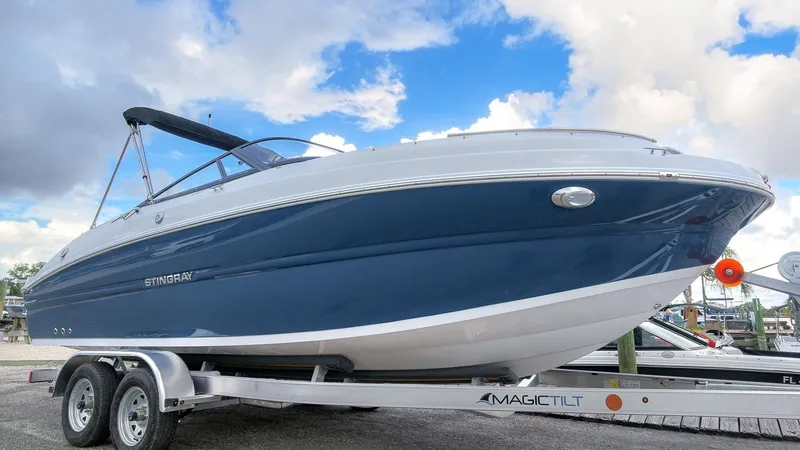 Slide: The Image of A blue and white 2027 Stingray 211 DC sits on a trailer under a cloudy sky. - 4