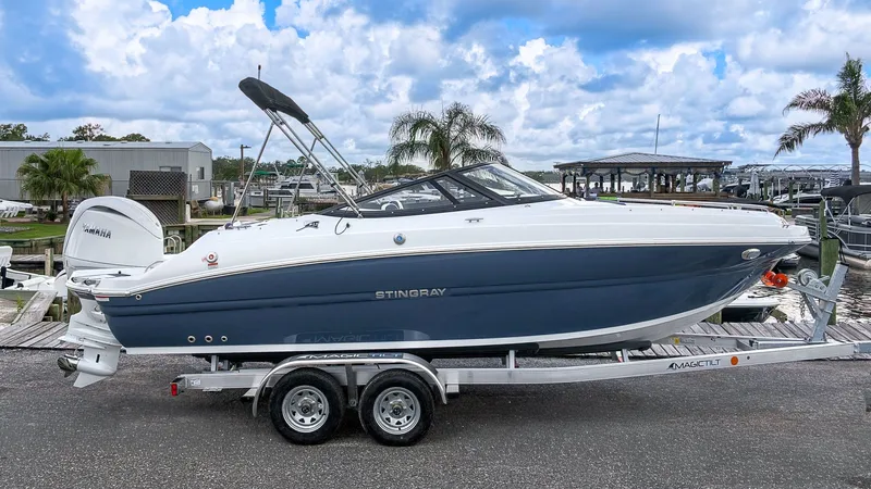 The Image of A 2027 Stingray 211 DC boat on a trailer, featuring a blue hull and white deck. - 1