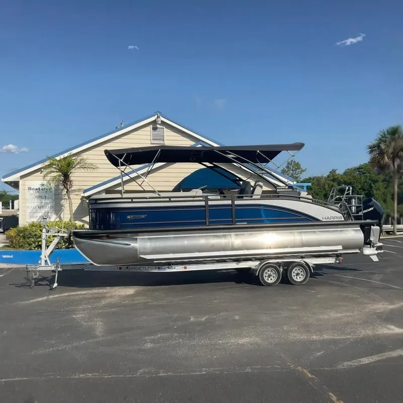 The Image of A 2025 Harris Solstice 250 SL pontoon boat on a trailer in front of a building. - 0