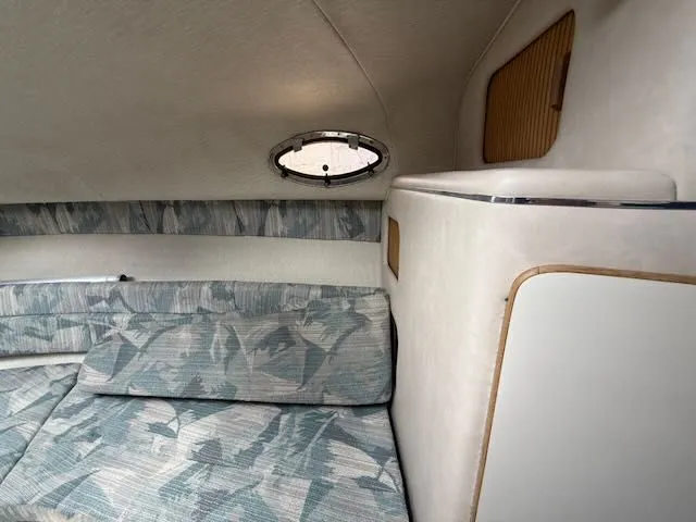Slide: The Image of Interior of a 1994 Sea Ray 270 with cushioned seating and a small porthole. - 16