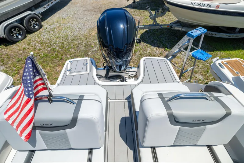 Slide: The Image of 2025 Chaparral 250 OSX boat with American flag and outboard motor, docked on grass. - 5