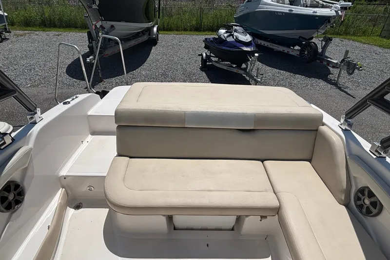 Slide: The Image of 2018 Regal 1900 ES Bowrider interior with beige seating, parked on gravel. - 16