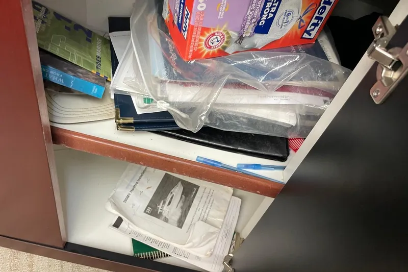 Slide: The Image of A cluttered cabinet with books, papers, and a box of trash bags, featuring Sea Ray 40 Motor Yacht brochure. - 24