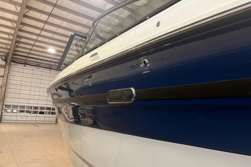 Slide: The Image of 2026 Sea Ray SDX 250 Surf boat in a warehouse, showcasing sleek blue and white design. - 2