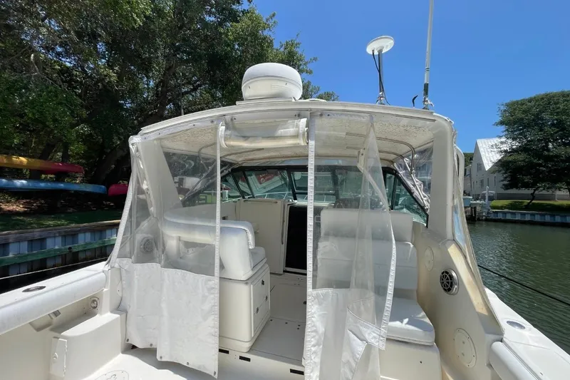 Slide: The Image of 1997 Tiara Yachts 3100 Open boat interior with clear curtains and seating, docked by trees. - 6