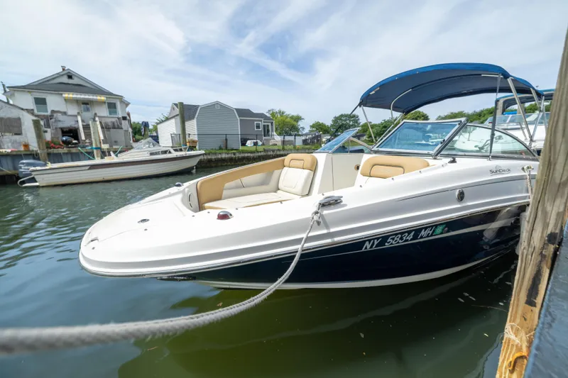 Slide: The Image of 2011 Sea Ray 220 Sundeck boat docked in a marina, featuring a blue canopy. - 2