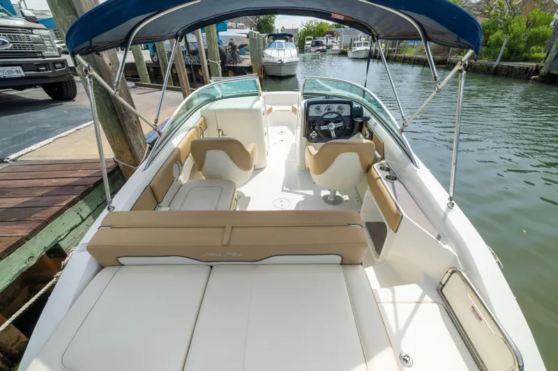 Slide: The Image of 2011 Sea Ray 220 Sundeck boat with tan seating and blue canopy docked by the water. - 26