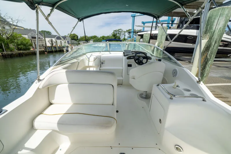 Slide: The Image of 2002 Searay 260 Sundancer boat interior with white seating and steering wheel, docked by the water. - 23