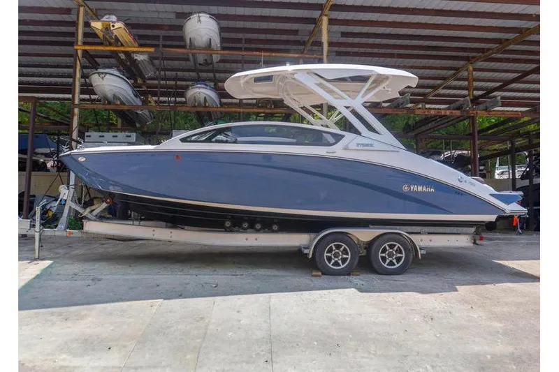 Slide: The Image of 2023 Yamaha Boats 275SDX in storage, sleek design, blue hull, dual-axle trailer. - 2