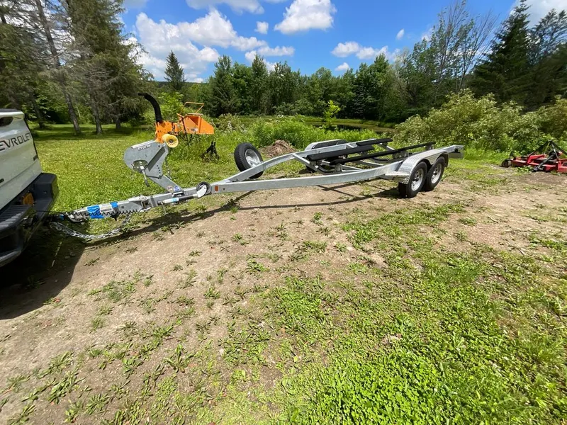 Slide: The Image of A boat trailer sits on a grassy field, surrounded by trees and a blue sky. - 30