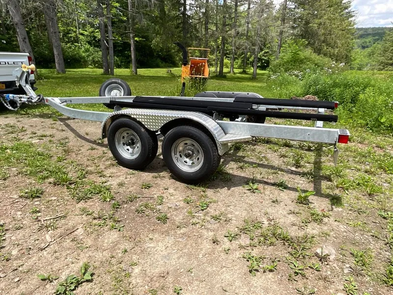 Slide: The Image of A boat trailer sits on grassy terrain, surrounded by trees and a vehicle. - 31