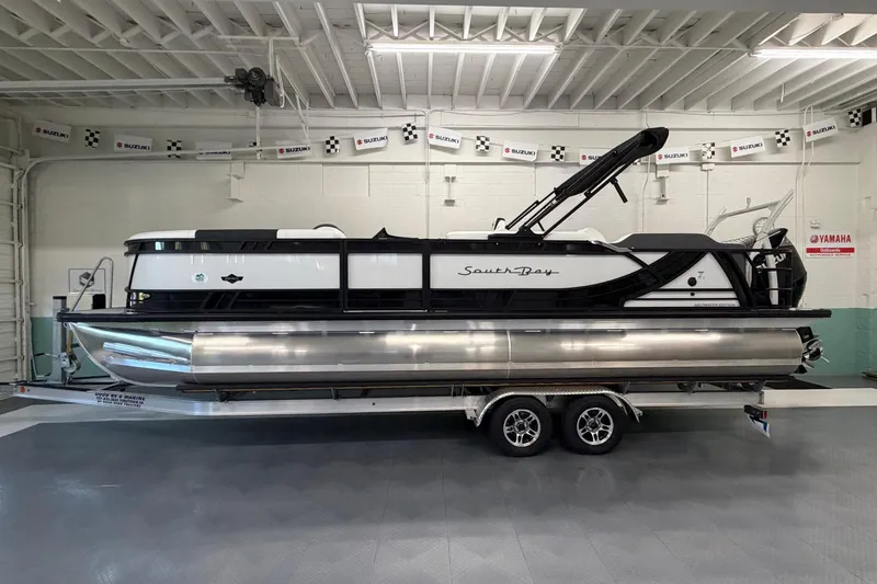 Slide: The Image of 2026 South Bay 525SB2 pontoon boat on trailer in showroom setting. - 1