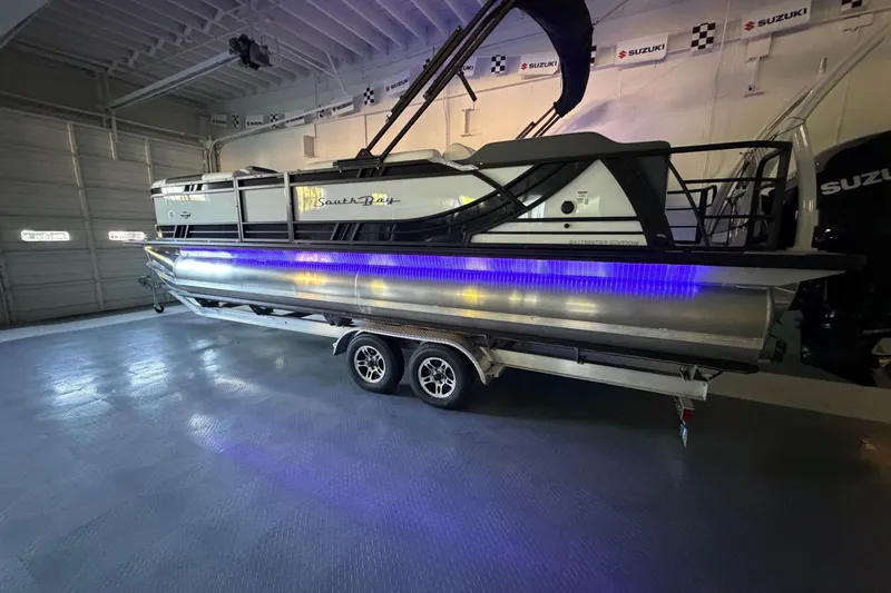 Slide: The Image of 2026 South Bay 525SB2 pontoon boat with blue LED lights in a showroom. - 21
