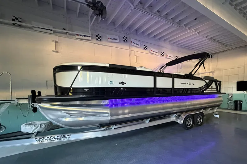 Slide: The Image of 2026 South Bay 525SB2 pontoon boat with blue LED lights on trailer indoors. - 28