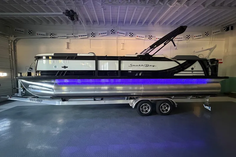 Slide: The Image of 2026 South Bay 525SB2 pontoon boat with blue LED lights on a trailer in a garage. - 35