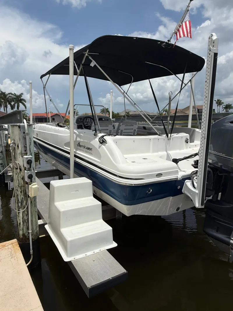 Slide: The Image of A 2022 Hurricane 231 SS boat on a lift, featuring a Bimini top and an American flag. - 2
