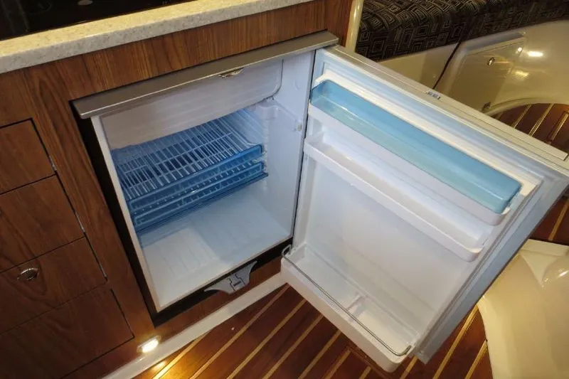 Slide: The Image of Open refrigerator inside 2010 Pursuit OS 345 Offshore boat, showcasing wooden cabinetry and interior design. - 17
