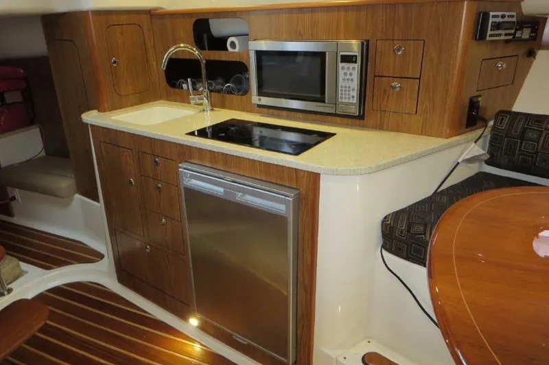Slide: The Image of 2010 Pursuit OS 345 Offshore boat interior with kitchenette, featuring sink, microwave, and wooden cabinetry. - 15