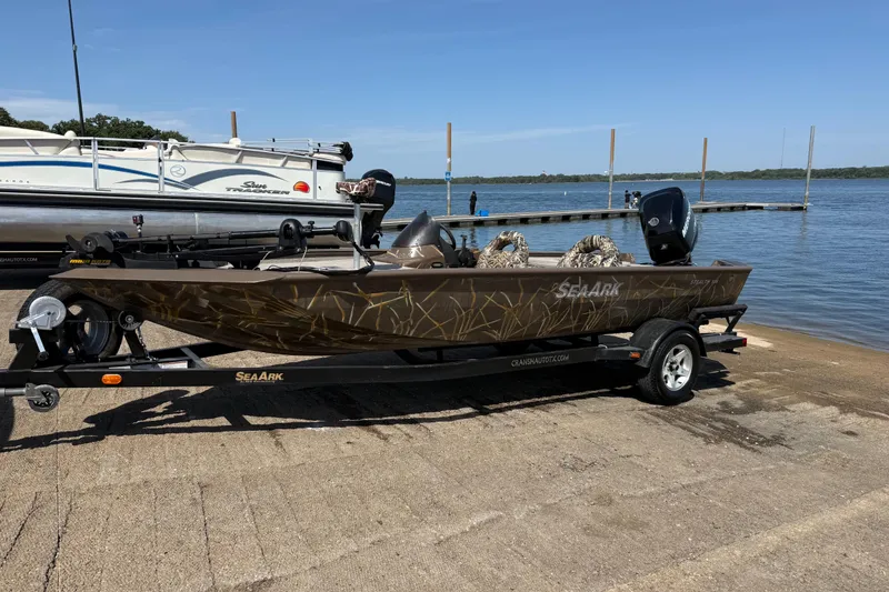 Slide: The Image of 2010 SeaArk Stealth 190 boat on trailer by lake, featuring camouflage design. - 2