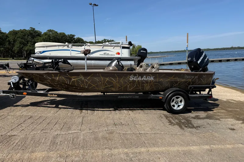 Slide: The Image of 2010 SeaArk Stealth 190 boat on trailer by lakeside, featuring camouflage design and Mercury engine. - 4
