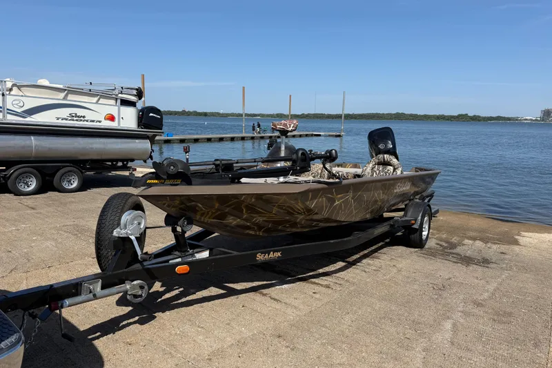 The Image of 2010 SeaArk Stealth 190 boat on trailer by a lake under clear blue sky. - 0