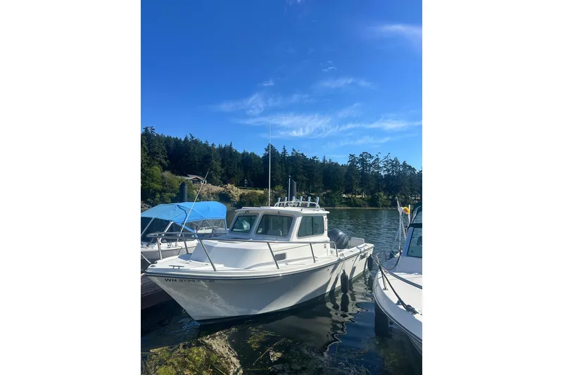 Slide: The Image of 2022 Parker 2120 Sport Cabin boat docked on a serene lake under a clear blue sky. - 1