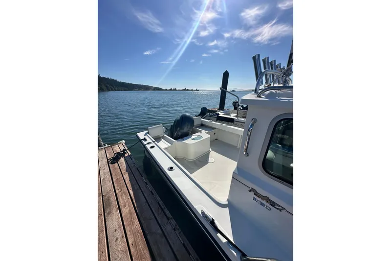 Slide: The Image of 2022 Parker 2120 Sport Cabin boat docked by a scenic lake under a clear blue sky. - 5
