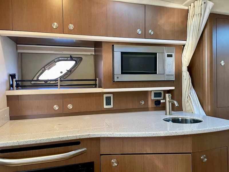 Slide: The Image of 2014 Sea Ray 330 Sundancer kitchen with microwave, sink, and wooden cabinetry. - 11