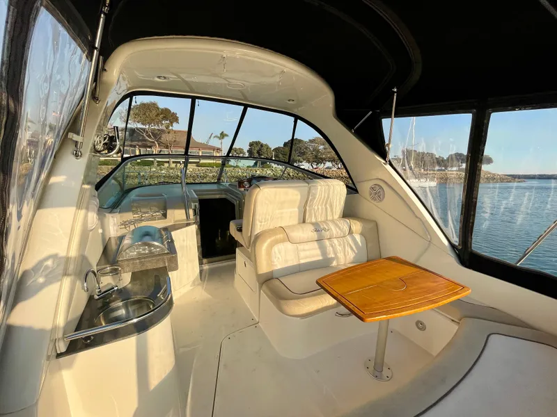 Slide: The Image of 2014 Sea Ray 330 Sundancer interior with seating, table, and helm, overlooking serene waters. - 42