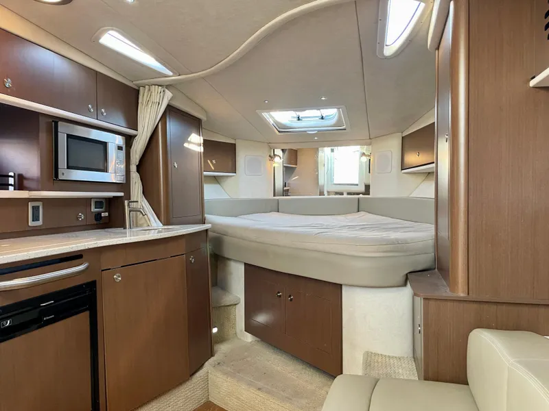 Slide: The Image of 2014 Sea Ray 330 Sundancer cabin interior with bed, kitchenette, and wood cabinetry. - 6