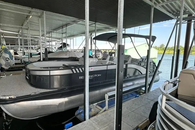 Slide: The Image of 2021 Bennington L Bowrider 25 Quad Bench pontoon boat docked under a covered marina. - 1