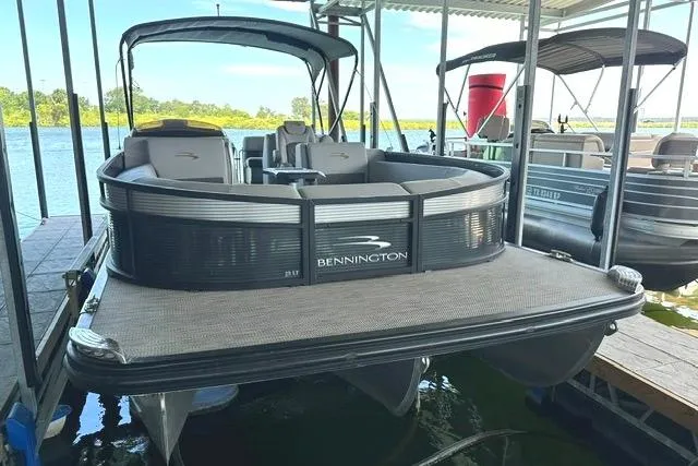 Slide: The Image of 2021 Bennington L Bowrider 25 Quad Bench pontoon boat docked on a sunny day. - 2